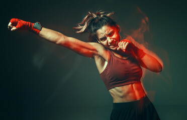 Cool girl fighter with relief abs makes jab in studio in neon light. Sport and motivation concept. Long exposure shot - obrazy, fototapety, plakaty