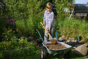 Boy working with the shovel and overloading the ground into the wheelbarrow