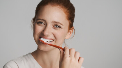 Attractive smiling girl happily looking in camera brushing teeth over white background