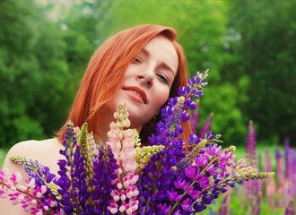 Beautiful redhead woman with vivid lupin bouquet in a field close-up