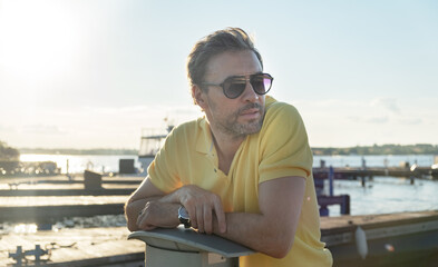 Fototapeta na wymiar Handsome good-looking mature man wearing sunglasses, yacht pier in marina at background. 