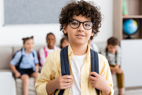 Selective focus of muslim schoolboy with backpack looking at camera in classroom