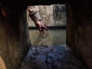 The reflection of a girl's hand fellon a water-filled cistern.