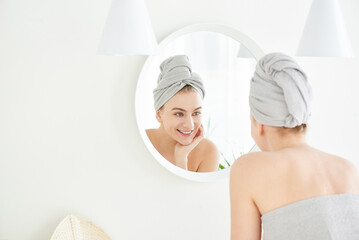Portrait of  young girl with  towel on head in white bathroom looks and touches her face in the...