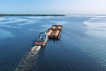 A large barge with sand sails along the coast along the wide Volga river