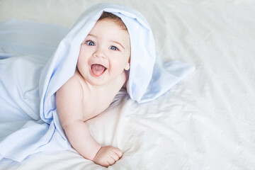 Newborn toddler boy laughing on the bed and looking at the camera