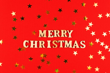 wooden letters on red background. Merry christmas lettering on red paper with scattered stars confetti. Festive greeting card.