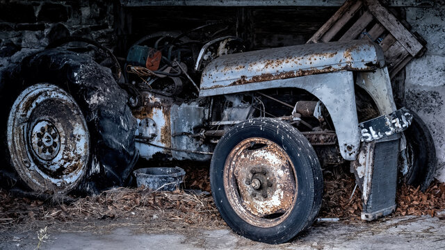 Old vintage tractor lying in disrepair and rotting in a dilapidated barn
