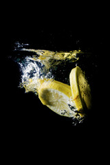 Fresh sliced lemon fruit splashing into clear water isolated black background 