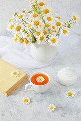 still life bouquet of field daisies in a vase, an old book and a cup of tea on a white background