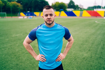 Serious sportsman looking at camera standing on green soccer field