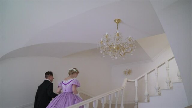 Couple holding hands while climbing stairs. A young couple in suits that were worn in the 19th century climb the stairs. A guy and a girl in karty outfits climb the stairs. 19th century clothes on a