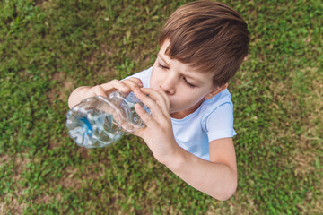Cute child drinks water from a bottle on the street in summer