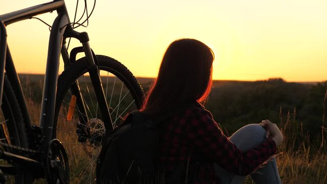 single woman cyclist resting in park. concept of adventure and travel. free girl travels with bicycle in sunset. Healthy young woman hiker sitting on hill next to bicycle, enjoying nature and sun.