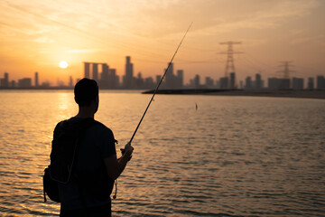 During the enchanting sunset, a young angler stands on the beach, casting their line while gazing...
