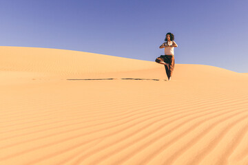 A youthful woman engages in a yoga practice amid the vast expanse of desert dunes in the United...
