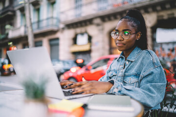 Focused young ethnic woman browsing laptop in street cafe