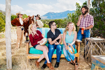 Fototapeta premium group of friends in south western theme in the outdoors camping, drinking, and sitting down on bench enjoying talking, laughing, fun and companionship playing music on a tamborine drum