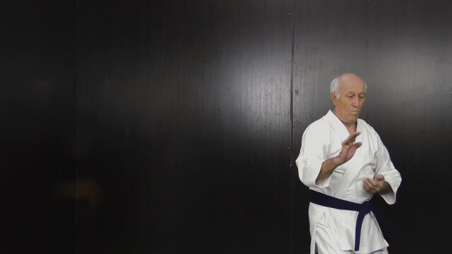 Old man athlete with blue belt performs formal karate exercises