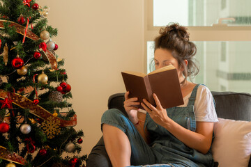 In the festive ambiance of Christmas, a young woman is immersed in a book while seated comfortably...