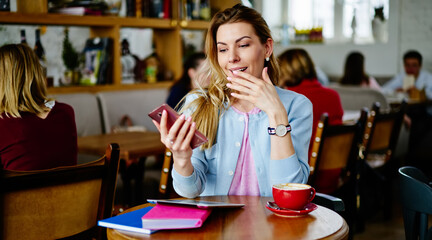 Young woman in cafe using smartphone covering mouth with hand