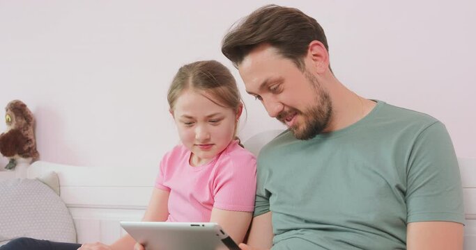 Father and teen daughter is sitting on the sofa, and looking at the photo album in tablet.