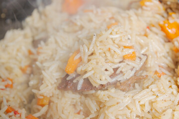 Cooking pilaf in a cauldron on the grill outside in the summer