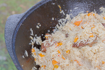 Cooking pilaf in a cauldron on the grill outside in the summer