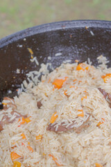 Cooking pilaf in a cauldron on the grill outside in the summer