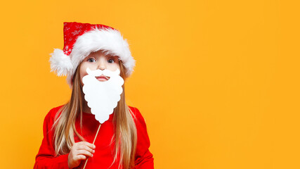 Fototapeta na wymiar Little Santa.Funny child girl in Santa red hat holding paper beard on blue background.