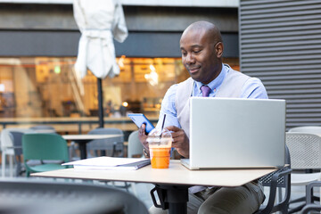 African American businessman using his smartphone while working remotely from a modern coffee shop. Space for text. 