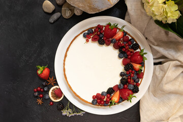 Homemade birthday cake cheesecake with protein cream garnished with fresh berries in a white plate on a black table