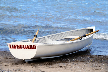 a white wooden lifeguard rescue row boat with oars ready on a sandy beach