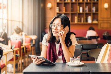 Happy Asian woman talking on the phone and using tablet computer in a coffee shop and background look old or vintage style.