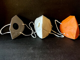 Three KN-95 face masks in white,grey and orange color. Isolated on black background. Protection from coronavirus or covid-19.Copy space. Front view