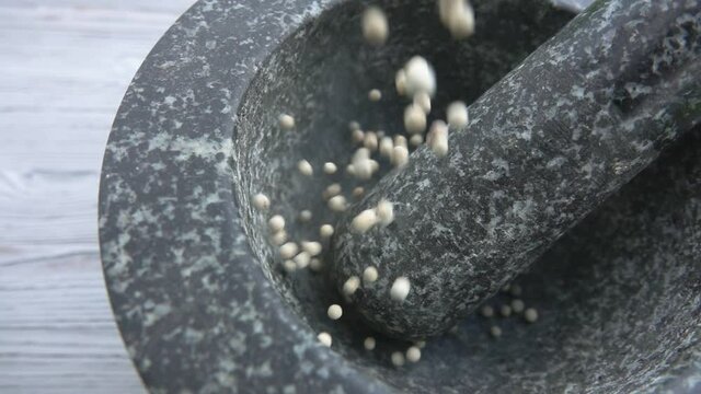 Close-up of white peppercorns falling into the grey stone mortar in slow motion
