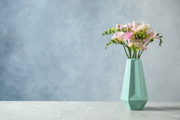 Beautiful blooming freesias in vase on table against blue background. Space for text
