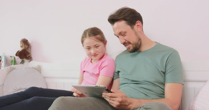 Father and teen daughter sitting on the sofa in living room, browsing the online store, enjoying weekend. Girl asks to buy something for her, but her father does not agree.