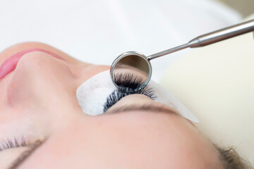 Eyelash extension procedure. Female eye with long eyelashes. Close up. mirror in the hands of the master
