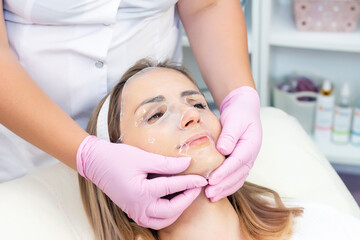 cosmetologist applies a hydrogel mask to a young woman on her face. The procedure by a beautician. Relax