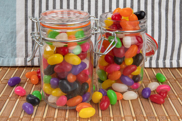two preserving jars of colorful jelly beans, one open, one closed, on a bamboo mat