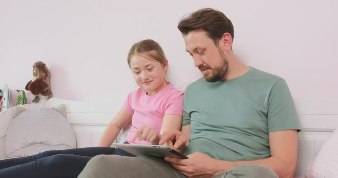 Father and teen daughter sitting on the sofa in living room, browsing the online store, enjoying weekend. Father asks what she thinks about some of articles.