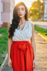 Fall fashion emotional brunette girl curly hairstyle in white poppy dress enjoying warm evening sun outdoors portrait small city street