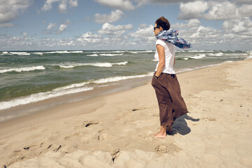 Lonely middle aged woman on the beach looking at sea on windy summer day