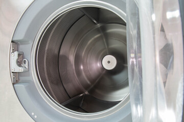 Opening front door of industrial laundry washing machine. Metal tub is inside. 
