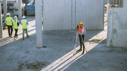 Construction Worker Using Theodolite Surveying Optical Instrument for Measuring Angles in Horizontal and Vertical Planes on Construction Site. Worker in Hard Hat Making Projections for the Building.