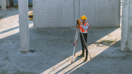 Construction Worker Using Theodolite Surveying Optical Instrument for Measuring Angles in Horizontal and Vertical Planes on Construction Site. Worker in Hard Hat Making Projections for the Building.