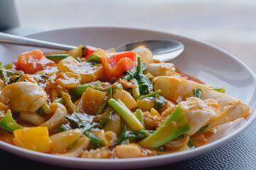Close up at Stir fried squid with salted egg yolk on white dish on black table background with nature light by window at seafood restaurant, Selective focus.