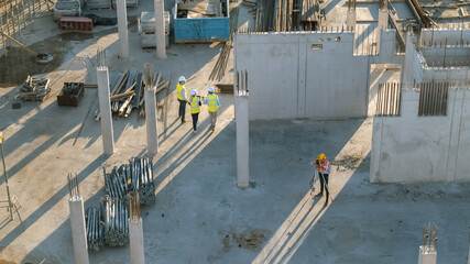 Aerial Shot of a New Constructions Development Site with Diverse team of Engineers and Architects Discussing Real Estate Projects. Heavy Machinery and Construction Workers are Working in the Area.