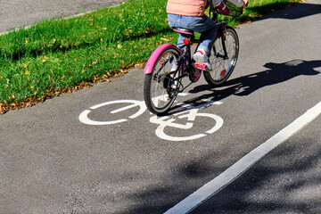The girl rides the pink bicycle on the bike path in autumn in sunny weather.